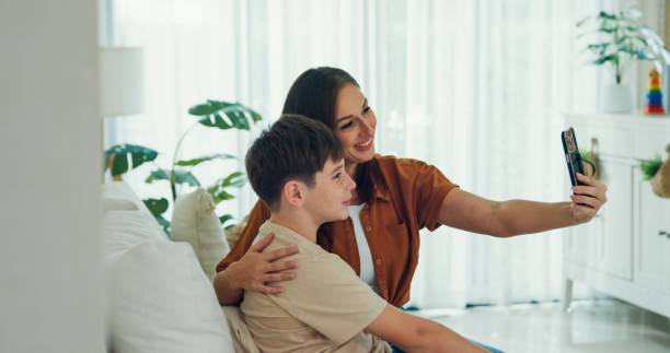 istock Young mother and her son sit on the sofa, smiling and taking a selfie together, capturing a joyful and bonding moment at home. Family moment. 2193515699