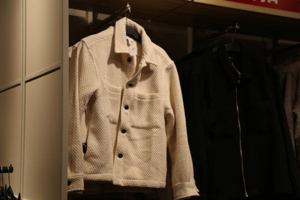 A white jacket hangs on a rack next to a black jacket. The white jacket is a knit jacket with buttons and a zipper