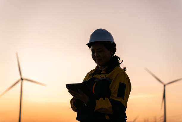 istock Asian Female Engineer Silhouetted Against Sunset Reviewing Data on Digital Tablet in Wind Farm, Nakhon Ratchasima, Thailand 2193523855
