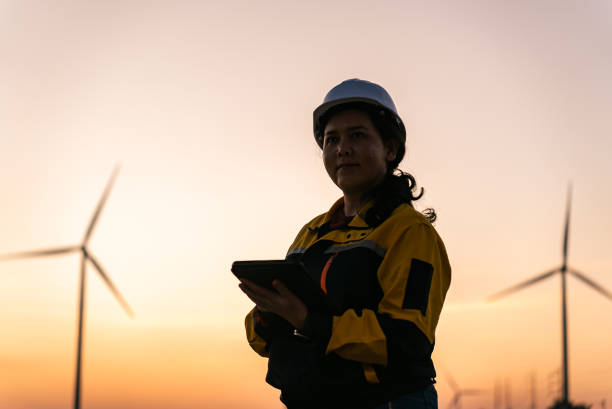 istock Asian Female Engineer Silhouetted Against Sunset Reviewing Data on Digital Tablet in Wind Farm, Nakhon Ratchasima, Thailand 2193523863