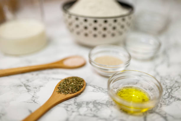 Various ingredients for crafting food including flour, milk, spices, and oil are displayed on a white marble surface, showcasing an arrangement suitable for homemade cooking and baking preparations