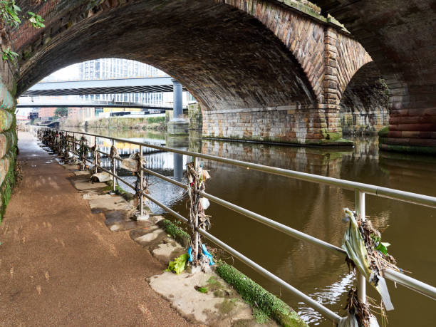 Urban riverside path under stone bridge with industrial backdrop. Salford, Manchester.