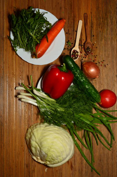 Close-up of a Senior Man 50+ in a Light Blue Shirt and Gray Apron Showing Bowls with Chopped Onion and Carrot. The Scene Focuses on the Ingredients, Highlighting the Freshness and Preparation for a Healthy Meal. The Careful Arrangement of the Chopped Vegetables in the Bowls Emphasizes the Precision and Care Taken in Cooking.