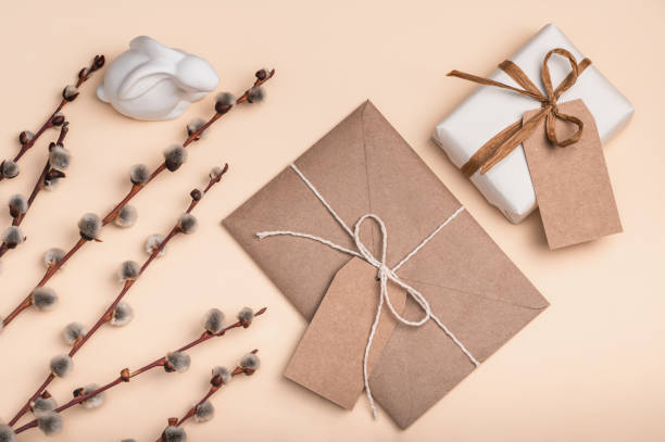 Gift box, envelope and blank label made of craft paper on a peach background with willow branches and Easter bunny. Easter card.