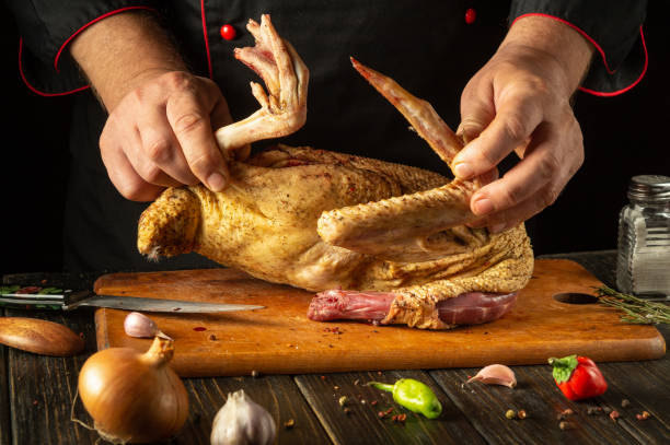 istock A skilled chef expertly handles a whole raw chicken, preparing it for cooking. Fresh ingredients like garlic and herbs surround the rustic wooden board, creating a culinary atmosphere 2193543983