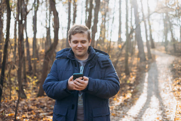 istock Adult 30s man hiker stand outdoors in a natural setting, smile while using his mobile phone outdoors. Hiking, lifestyle, adventure and tourism concept. 2193544515