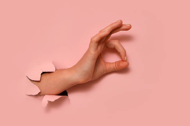 istock Hand showing OK gesture through torn hole in pink paper background. Conceptual studio shot for design and advertising. 2193546227