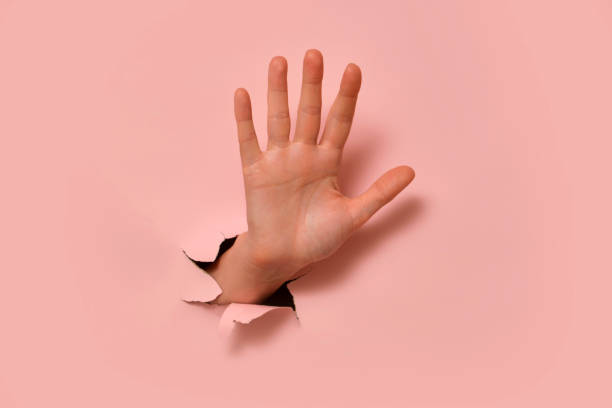 istock Human hand reaching through torn pink paper. Conceptual image with minimalistic background. Creative design element for banner and poster. 2193546233