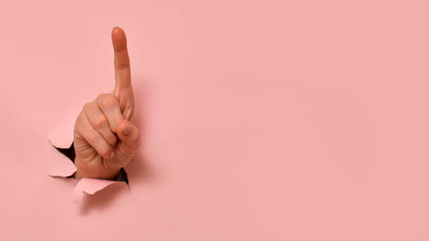 istock Hand showing index finger gesture through torn paper on pink background. Minimalist conceptual photography with copy space. 2193546234