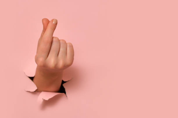 istock Hand making finger heart gesture through torn pink paper. Minimalistic composition with copy space. Love and affection concept for design and print. 2193546237