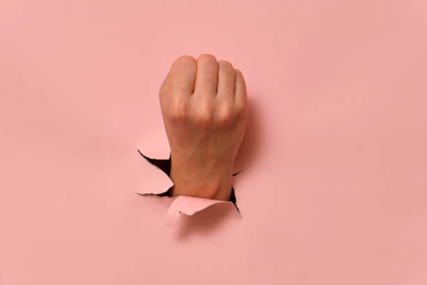 istock Hand breaking through pink paper wall with clenched fist. Conceptual studio shot for creative design. 2193546244