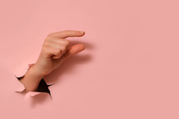 istock Hand making small gesture through torn hole in pink paper. Minimalist abstract concept. 2193546256