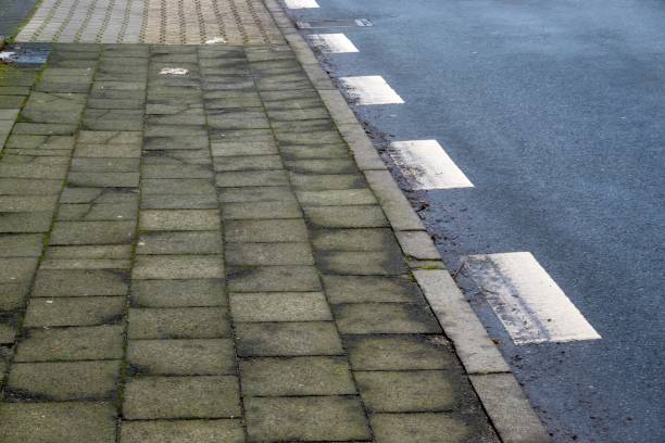 istock Damaged sidewalk tiles by the road with white lines 2193551390