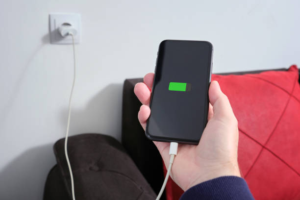 istock A man holds a smartphone in his hand, connected cable to a charger from electrical socket. Against the background of a residential apartment. 2193552621