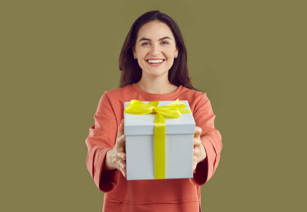 istock Smiling brunette woman in red sweatshirt is giving a present pulling hands on khaki background. 2193553571