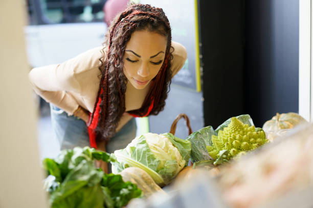 A young woman with beautifully braided hair leans over a vibrant display of fresh vegetables, showcasing her deep connection to the world of healthy eating and a nutritious lifestyle