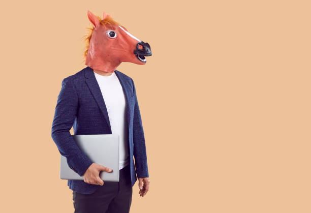 istock Freak bizarre anonymous guy with horse head holding laptop isolated on beige background. 2193559963