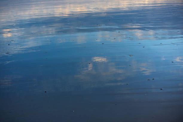 Idyllic scene with the shallows of the sea reflecting the sky and surf breaking in the distance.