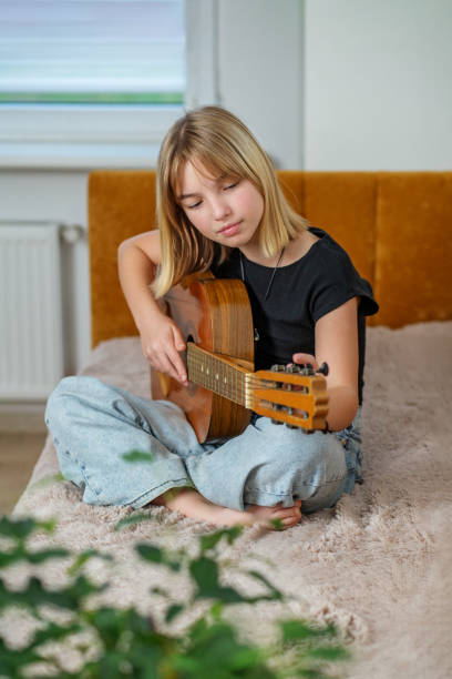 istock Girl playing guitar while sitting on bed in cozy room 2193564064