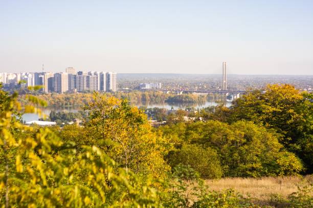 istock Panoramic view of autumn landscape with dense yellow-orange tree canopy, reflective water body separating urban area and natural scenery under clear blue sky 2193564607