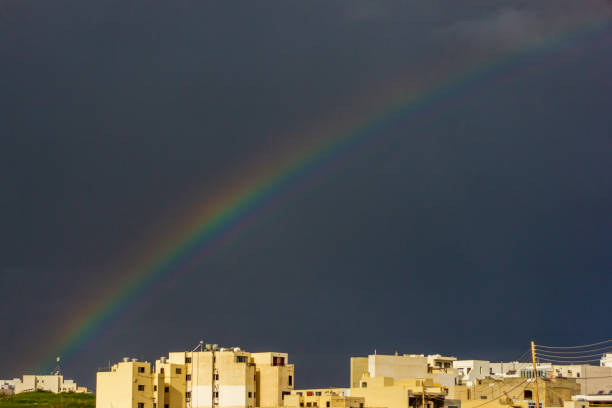 Bright and colorful rainbow spanning across a dim dramatic sky over urban apartment buildings.