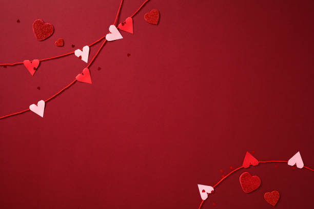 istock Valentine's Day background with red and pink paper hearts on strings, and scattered glitter hearts on a deep red backdrop 2193568894