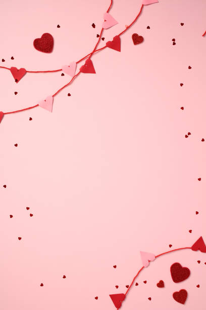 Valentine's Day background with red and pink heart-shaped decorations on a pink surface. Perfect for romantic, love-themed projects and celebrations