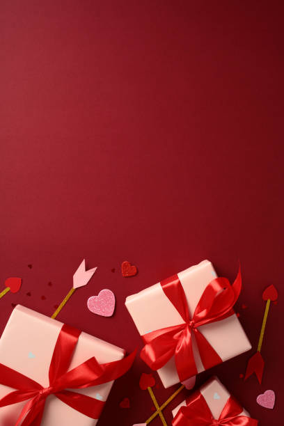 istock Valentine's Day vertical background with pink gift boxes wrapped in red ribbons, surrounded by decorative hearts and Cupids arrows. Perfect for romantic holiday promotions and celebrations 2193569151