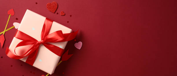 istock Gift box with red ribbon on red background, surrounded by heart-shaped decorations and Cupid's arrows. Valentines Day banner template. 2193569231