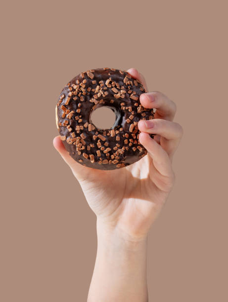 istock Hand holding tglazed chocolate donut on mocha brown background. 2193569339