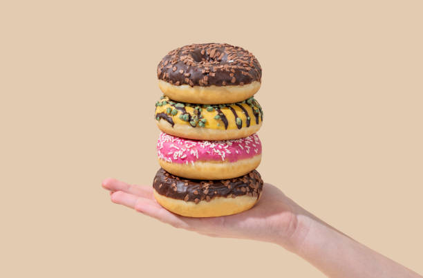 istock Hand holding stack of glazed donuts with different toppings on beige background. 2193569350