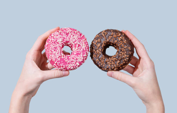 istock Hands holding two glazed chocolate and pink donuts on blue background. 2193569392