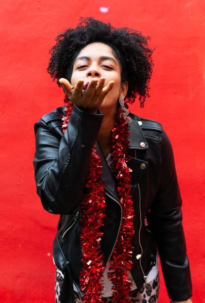 Young woman joyfully blowing confetti towards the camera, celebrating at a lively carnival party with a festive atmosphere