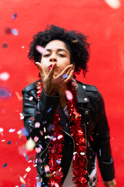 istock Young woman blowing confetti at party with red background 2193574466