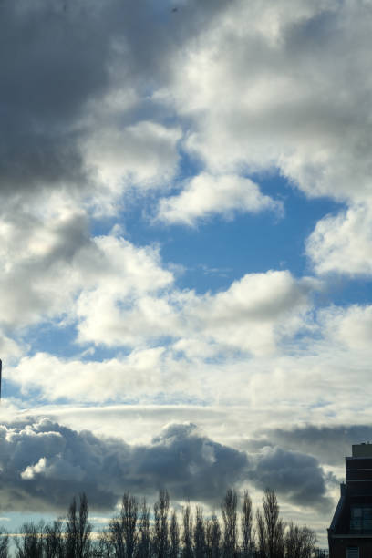 Cloudy sky with a patch of blue during daytime, seen above buildings and trees