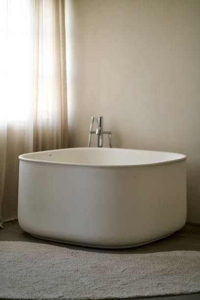 istock Modern white bathtub stands in a bright bathroom next to a window 2193575175