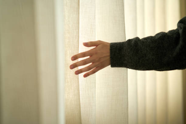 Hand touching white curtain in sunlight, feeling the fabric texture