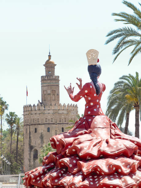 Seville, Spain - April 17, 2024 : Statue of a flamenco dancer in a red polka-dot dress, in front of the emblematic Torre del Oro during the Seville Fair.