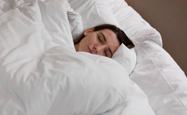 istock Young woman peacefully sleeping under white fluffy blankets in a cozy bed 2193578853