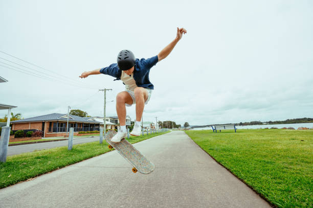istock Young skateboarder in protective helmet performing a trick mid-air on a sidewalk in a park, showcasing agility and outdoor adventure 2193578917