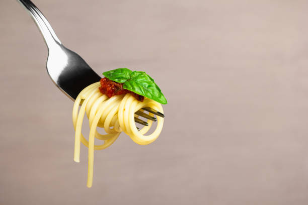 istock Fork of spaghetti with tomato sauce, cheese, and basil on beige background. Close up. 2193582049