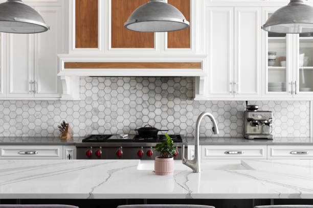 istock A white kitchen with marble countertop, steel pendant lights, and hexagon tile backsplash. 2193586436