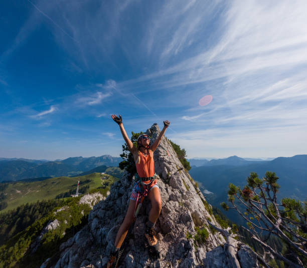 Adventurer raises arms in victory on rocky summit. Solo hiker enjoying breathtaking mountain views. Outdoor enthusiast celebrating a successful climb in nature.