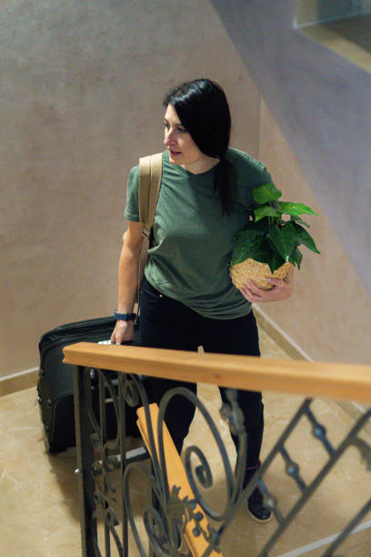 Woman with suitcase, backpack and plant moving from apartment.
