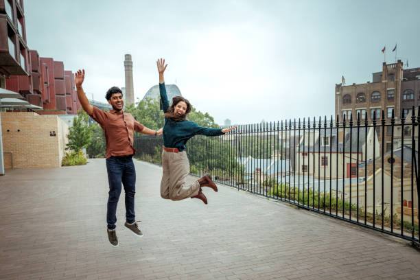Cheerful casually clothed couple jumping together while enjoying cloudy day in Sydney