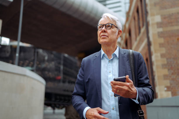 istock Well dressed senior man using smart phone while walking at the city downtown 2193590578