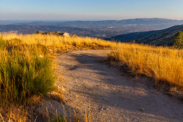 istock A dirt path winds through golden grass on a hilltop overlooking a distant valley and mountains under a clear sky 2193592035