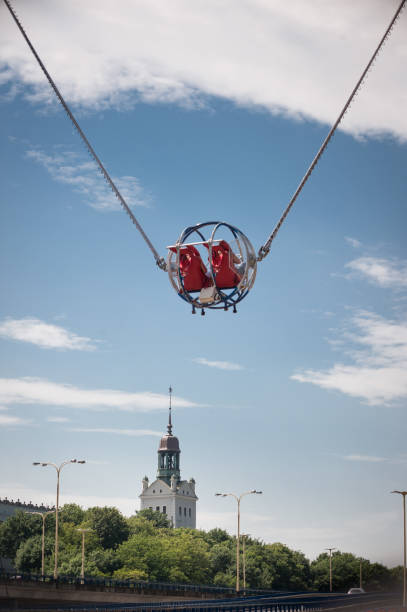Bishkek, Kyrgyzstan - June 1, 2025: A moment on a catapult ride at an amusement park where two young women sit upside down in a spherical cage against the sky with their arms raised in delight, their hair flying. A thrilling ride for adults and teenagers.