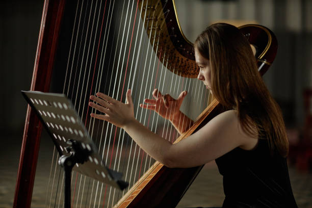 istock Young Woman Strumming Harp Strings Playing Classical Music in Dim Light Indoors 2193593621