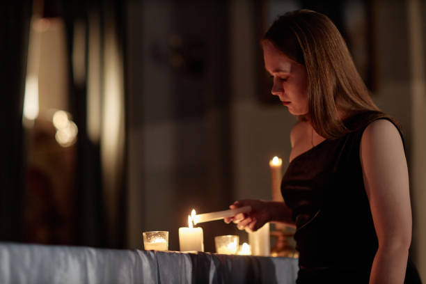 Medium shot of young woman in black dress lighting candle while praying in church service, copy space